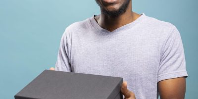 Excited african american man carrying a black giftbox, delighted by the unboxing experience. Happy male individual holding a package, feeling thrilled about receiving a delivery.
